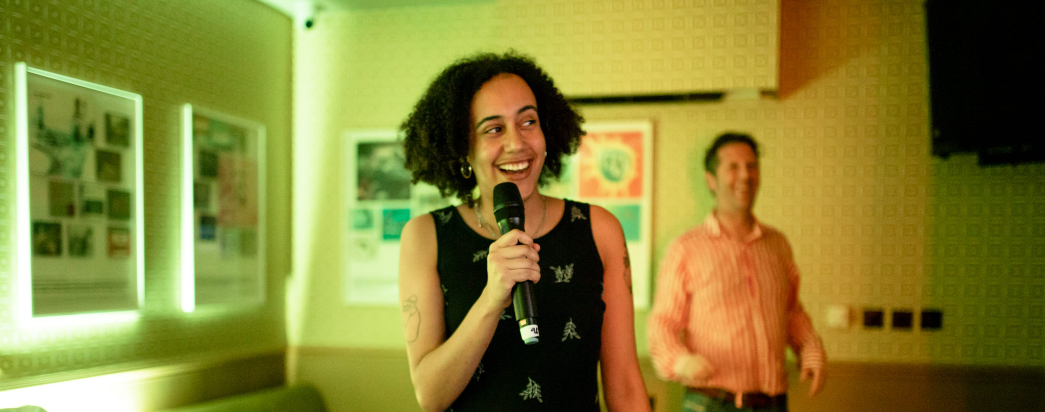 A woman singing in the 90s themed karaoke pod with the music through the ages exhibition in the background at The Old Grindstone pub